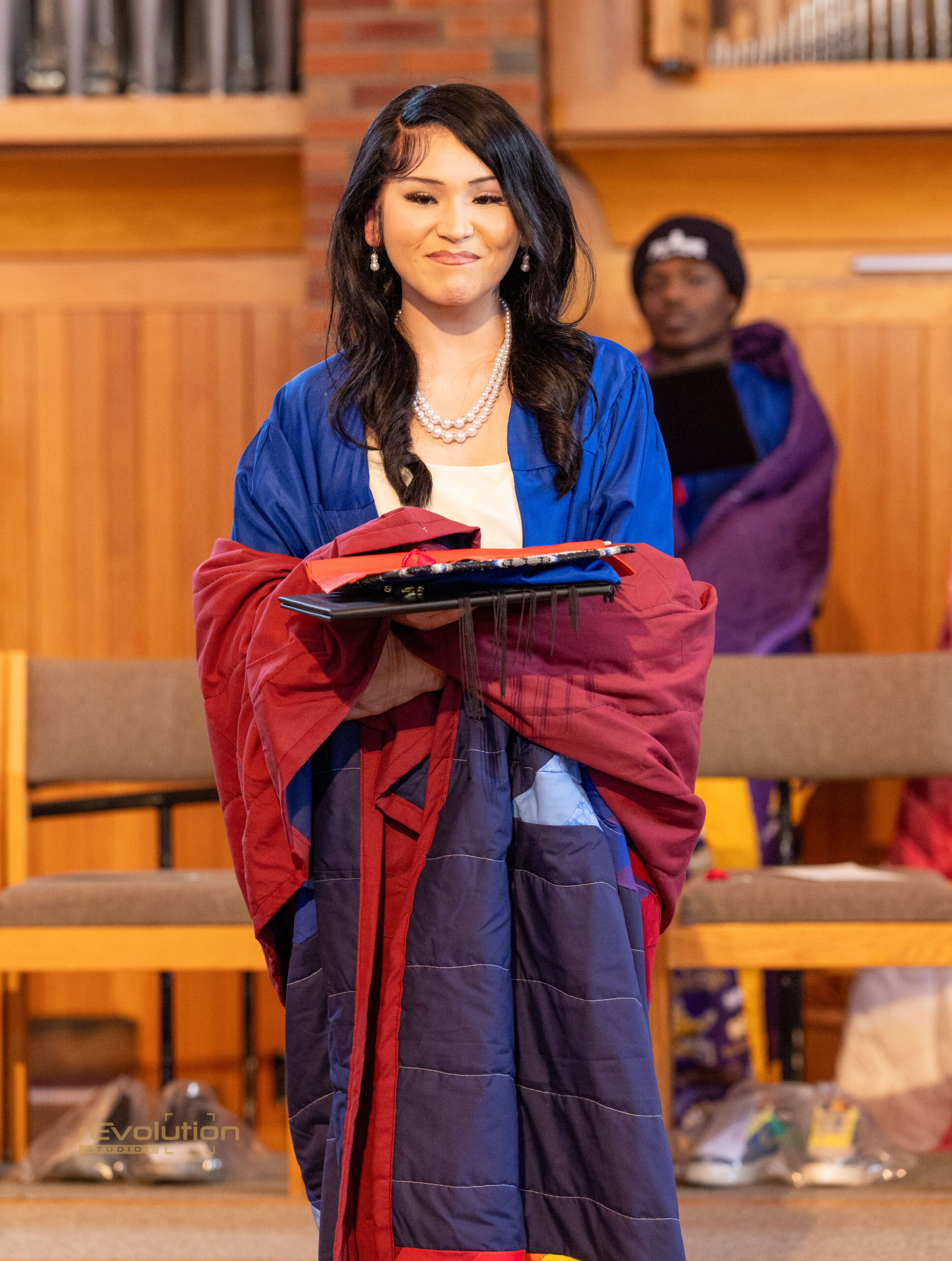 AFA Native graduate wearing graduation regalia and holding a handmade quilt